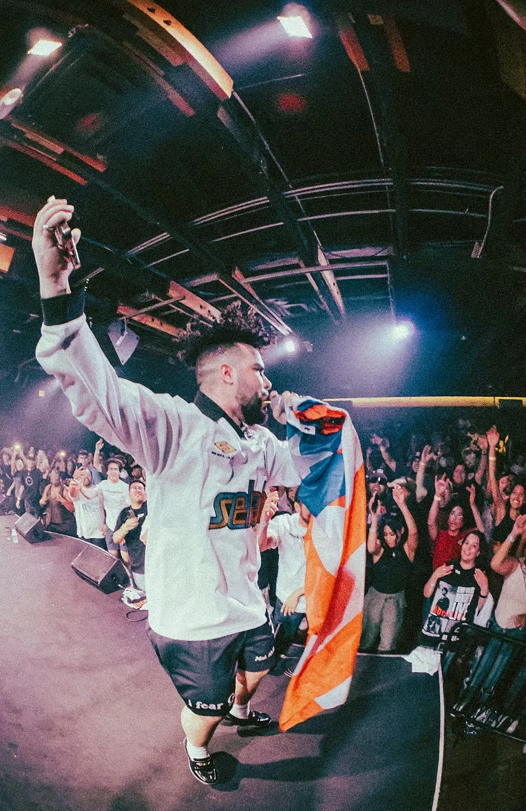 Kenny Rivers performing with a Puerto Rican flag in front of a cheering audience